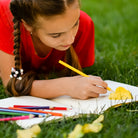 Girl lying on grass drawing in sketchbook  with colored pencils