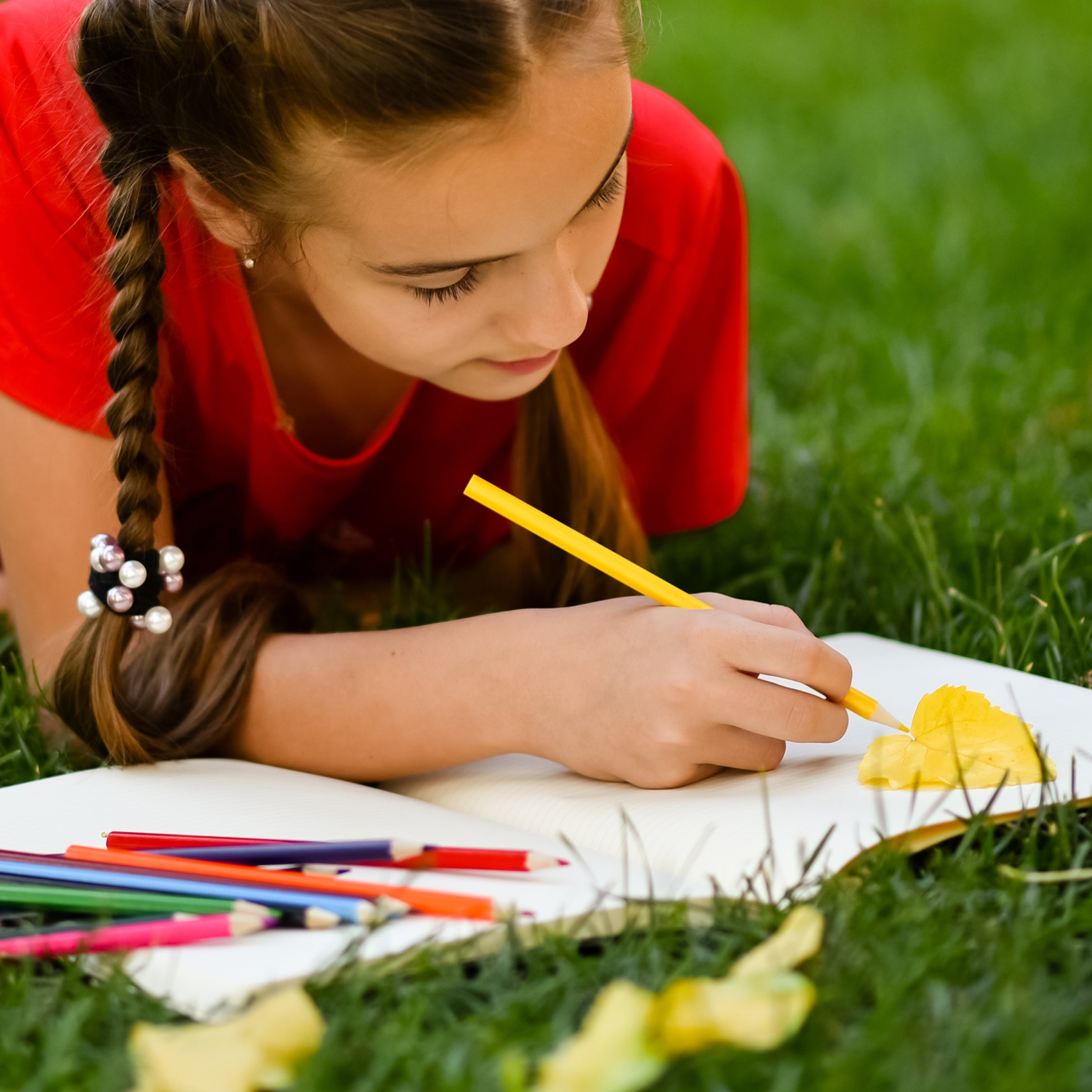 Girl lying on grass drawing in sketchbook  with colored pencils