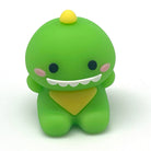 A small green dinosaur pencil sharpener with a yellow spike, yellow bandana, pink cheeks, and a wide white grin, photographed on a plain white background.