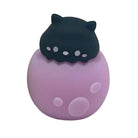 A small black cat in a purple spotted egg shape pencil sharpener with pink spots on a white background