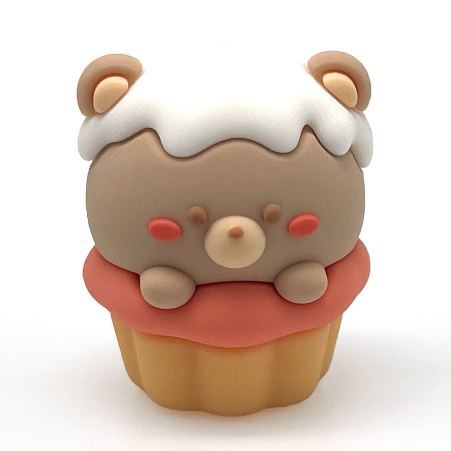 A small cupcake-shaped pencil sharpener with a light brown bear face and white frosting, and a yellow cupcake base, centered on a plain white background.