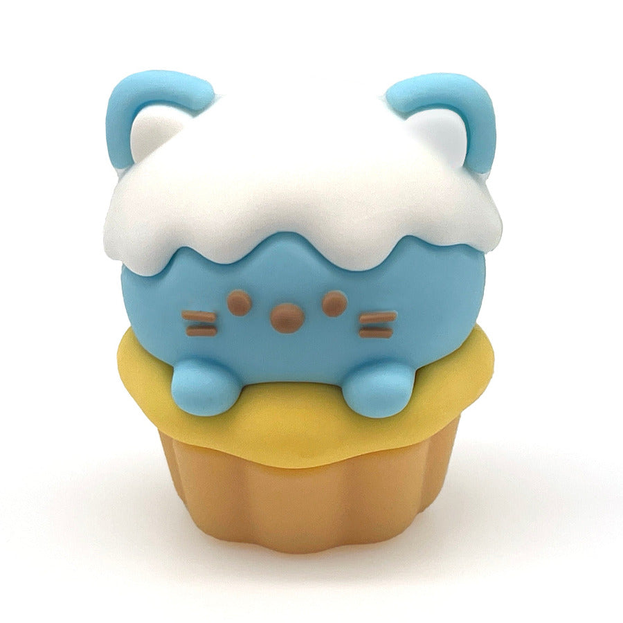 A small cupcake-shaped pencil sharpener with a light blue cat face and body, white frosting, and a yellow cupcake base, centered on a plain white background.