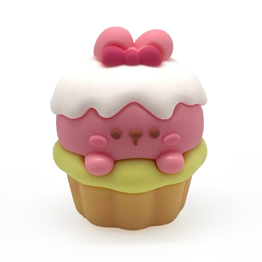 A cute, stylized cupcake pencil sharpener with a pink bunny face peeking out from white frosting, topped with a pink bow, sitting on a light green frosting layer over a tan base, set against a plain white background.