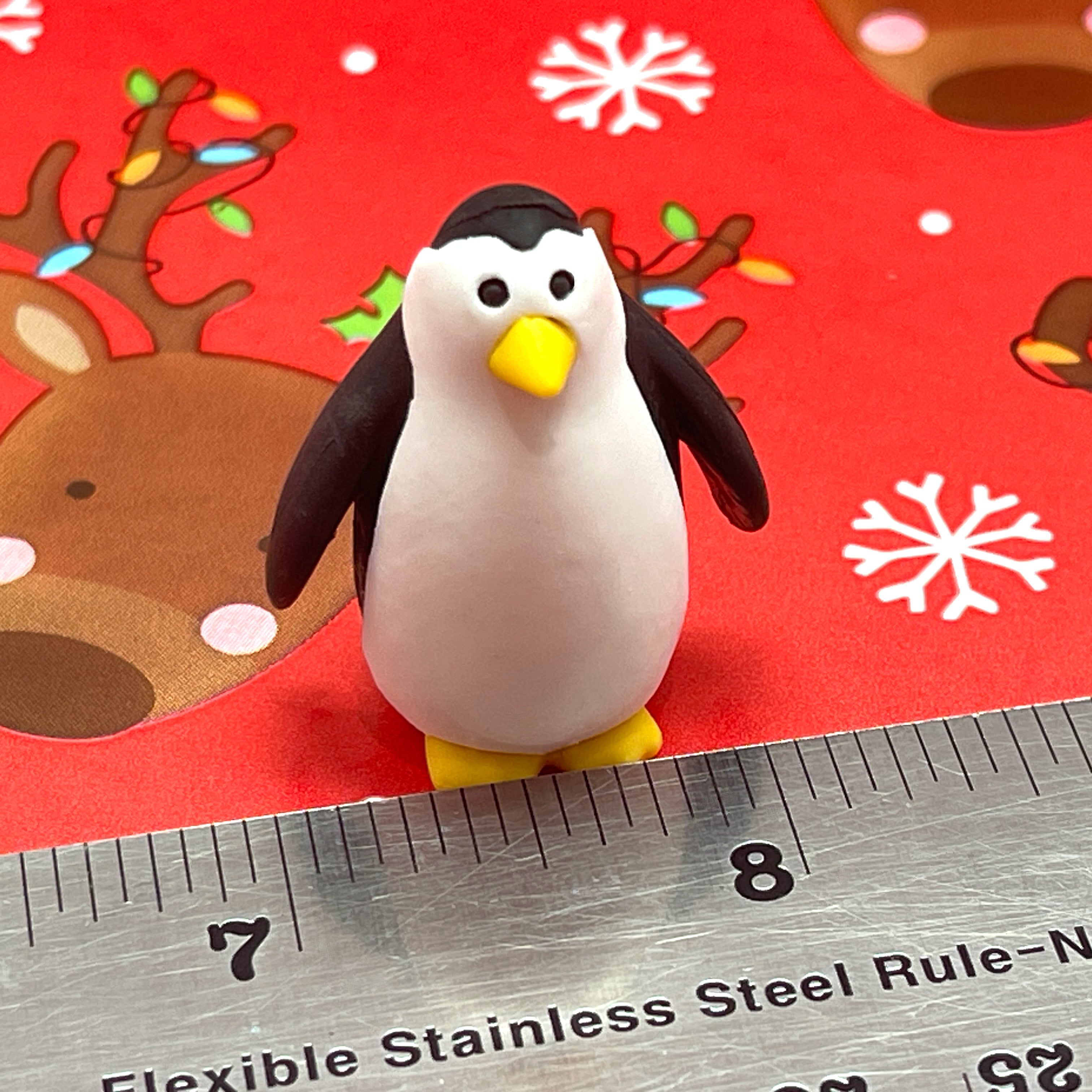 Penguin eraser on a red background with reindeer and snowflakes, next to a ruler for scale.
