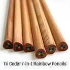 six cedar wood rainbow pencils fanned out on a white background, with text at the bottom reading 'Tri Cedar 7-in-1 Rainbow Pencils'. The triangular shape pencils show natural wood grain and the magic swirl multi-color rainbow core detail visible at the ends.
