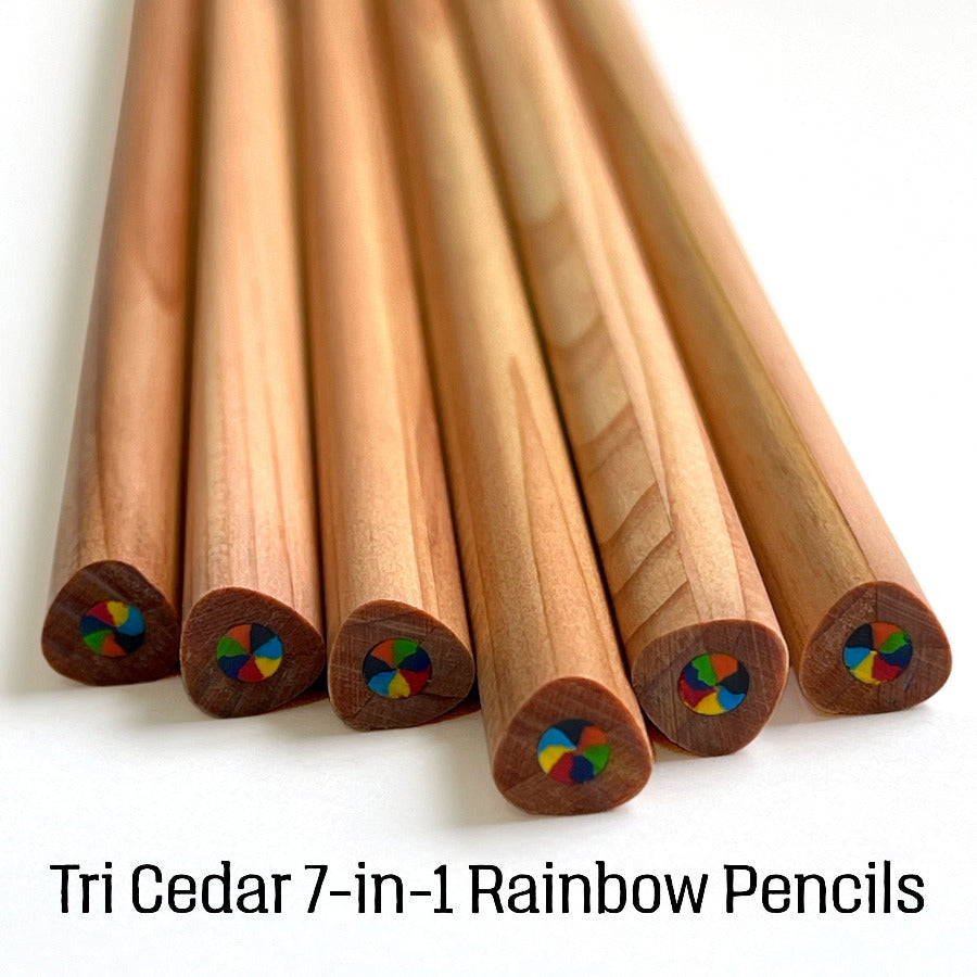 six cedar wood rainbow pencils fanned out on a white background, with text at the bottom reading 'Tri Cedar 7-in-1 Rainbow Pencils'. The triangular shape pencils show natural wood grain and the magic swirl multi-color rainbow core detail visible at the ends.