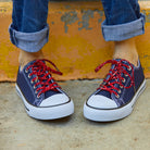 Navy sneakers with red laces worn with rolled-up jeans against a yellow wall.