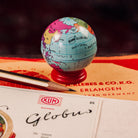 Small retro style world globe pencil sharpener on top of a KUM Globus box with a blurred background sitting next to a sharpened pencil.