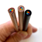 Detail image of hand holding 3 rainbow pencils and showing the 7-in-1 multi-color rainbow core against a white background.